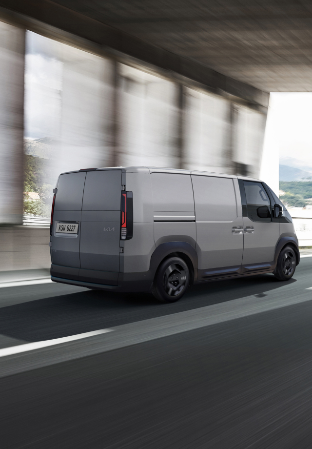 Rückansicht des Kia PV5 Cargo, der auf der Autobahn fährt – mit einem weiteren Kleinbus voraus.